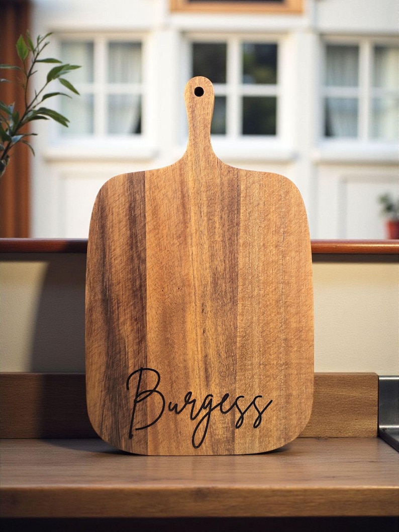 A wooden cutting board with the word "Burges" written on it, placed on a wooden surface.