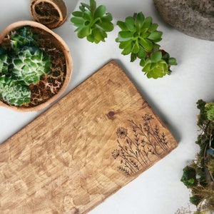May include: A wooden serving board with a natural wood grain finish and a design of stylized flowers etched into the surface.