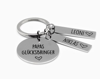 May include: Silver keychain with a round charm that says "Papas Glücksbringer" with a heart. Two smaller charms with the names "Leoni" and "Niklas" with hearts.