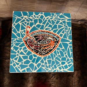 Op de afbeelding: Een mozaïek tafelblad met een blauwe achtergrond en een rood, oranje en zwart ontwerp van een kom met een werveling erin.