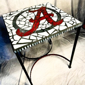 Könnte beinhalten: Ein kleiner, quadratischer Beistelltisch mit einer Mosaiktischplatte, die das 'A'-Logo der University of Alabama in Rot und Weiß zeigt. Der Tisch hat ein schwarzes Metallgestell.