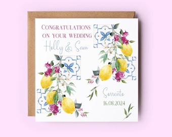 May include: A white wedding card with a watercolor illustration of lemons, flowers, and blue and white tiles. The text reads "Congratulations on your wedding Holly & Sam Sorrento 16.08.2024".