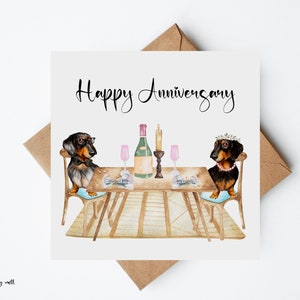May include: A square greeting card with a watercolor illustration of two dachshunds at a table set for a romantic dinner. The card reads "Happy Anniversary" in elegant script. A brown envelope is behind the card.