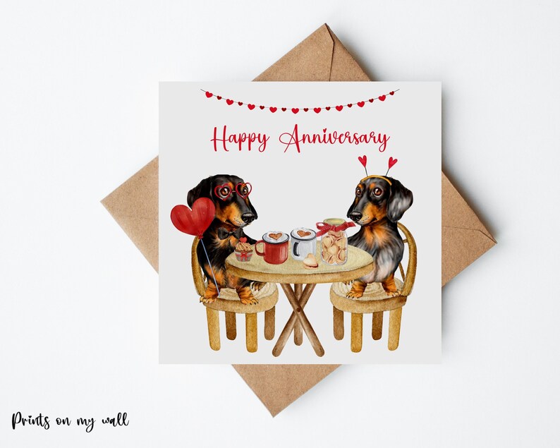 May include: A greeting card with a watercolor illustration of two dachshund dogs wearing party hats and glasses, sitting at a table with coffee and cookies. The card reads "Happy Anniversary".