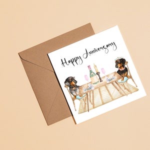 May include: A greeting card with a watercolor illustration of two dachshunds at a table set for a celebration. The card reads "Happy Anniversary" in elegant script. A brown envelope is next to the card.