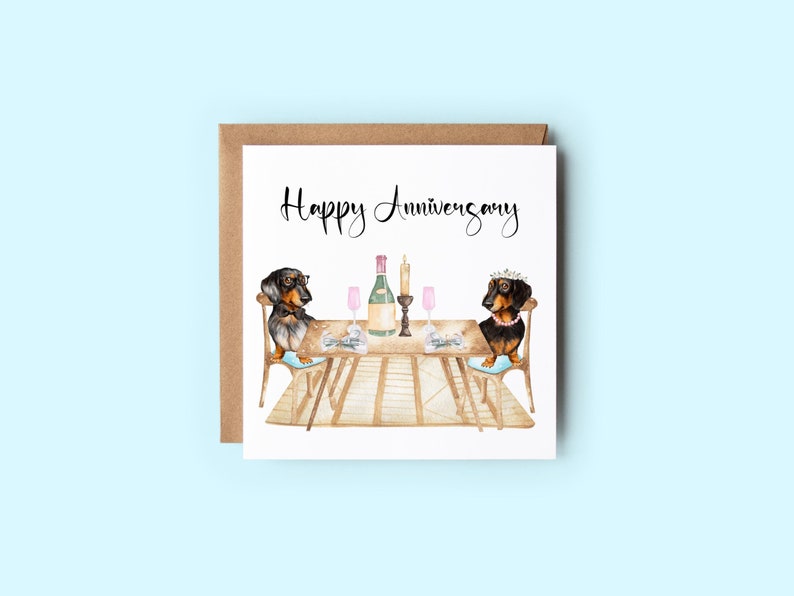 May include: A square greeting card with a brown envelope. The card features a watercolor illustration of two dachshunds at a table set for a romantic dinner. The words "Happy Anniversary" are written in elegant script.