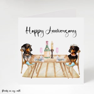 May include: A greeting card with a watercolor illustration of two dachshunds at a table set for a romantic dinner. The card reads "Happy Anniversary" in elegant script. The dogs are dressed up and there is a bottle of wine and candles on the table.
