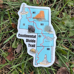 May include: A white sticker featuring a map of the Continental Divide Trail, with illustrations of landmarks and a bear. The sticker includes the text "Continental Divide Trail" and state abbreviations.