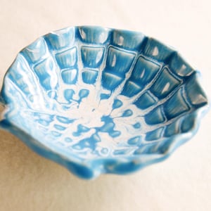 May include: A small, blue and white ceramic bowl with a scalloped edge. The bowl has a marbled design and a textured surface.