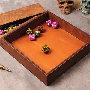 May include: A wooden box with a hinged lid, containing a collection of colorful dice. The box has a brown leather interior and is perfect for storing and rolling dice.