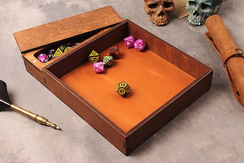 May include: A wooden box with a hinged lid, containing a collection of colorful dice. The box has a brown leather interior and is perfect for storing and rolling dice.