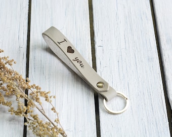 May include: A light gray leather keychain with a silver key ring. The keychain has the words "I love you" engraved on it with a small heart symbol.