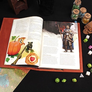 May include: An open book with a brown leather cover. The book has illustrations of a pumpkin, a squirrel, and a pie. The book is open to a page with text about a human character. There are dice and small glass jars with cork tops on a black surface.