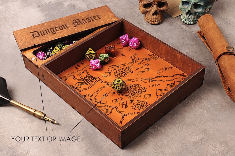 May include: A wooden box with a lid that says "Dungeon Master" on it. The box is open and has a brown leather map inside with dice on top of it.