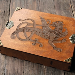 May include: A wooden box with a carved griffin design and brass hinges. The box has a dark brown stain and is closed.