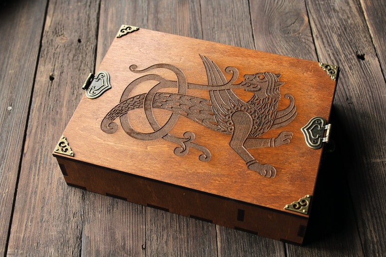 May include: A wooden box with a carved griffin design and brass hinges. The box has a dark brown stain and is closed.