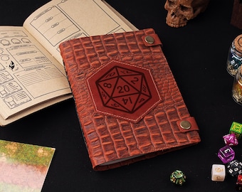 May include: A brown leather journal with a crocodile pattern and a red leather patch with a 20-sided die engraved on it. The journal is closed and lying on a black surface.