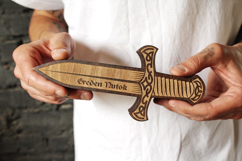 Pode incluir: Uma espada de madeira com um design de n&oacute; celta e a inscri&ccedil;&atilde;o "Greden Nutek".