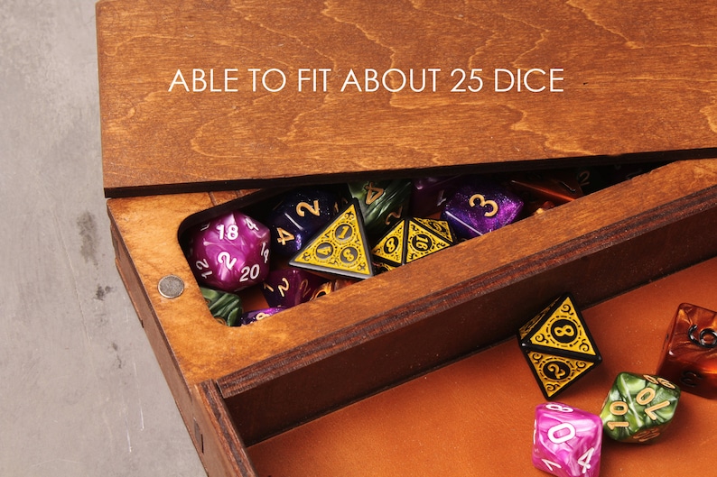 May include: A wooden box with a hinged lid, open to reveal a collection of colorful dice. The lid has the text "ABLE TO FIT ABOUT 25 DICE" engraved on it. The box is filled with dice of various colors, including purple, green, and black.