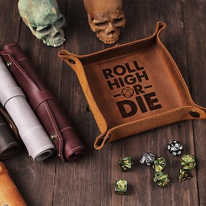 Può includere: Un vassoio da gioco in pelle marrone con la scritta "Roll High or Die" e un simbolo di dado. Il vassoio è su una superficie di legno con dadi e altri accessori da gioco.