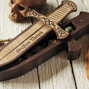 Pode incluir: Uma caixa de dados de madeira em forma de espada com uma tampa articulada. A tampa &eacute; gravada com um desenho de n&oacute; celta e as palavras "Greeden Nurtsk". A caixa est&aacute; aberta e cheia de dados verdes.