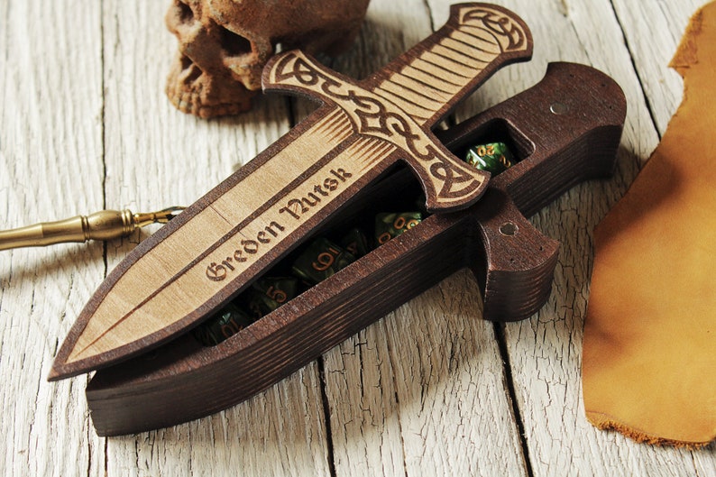 Pode incluir: Uma caixa de dados de madeira em forma de espada com uma tampa articulada. A tampa &eacute; gravada com um desenho de n&oacute; celta e as palavras "Greeden Nurtsk". A caixa est&aacute; aberta e cheia de dados verdes.