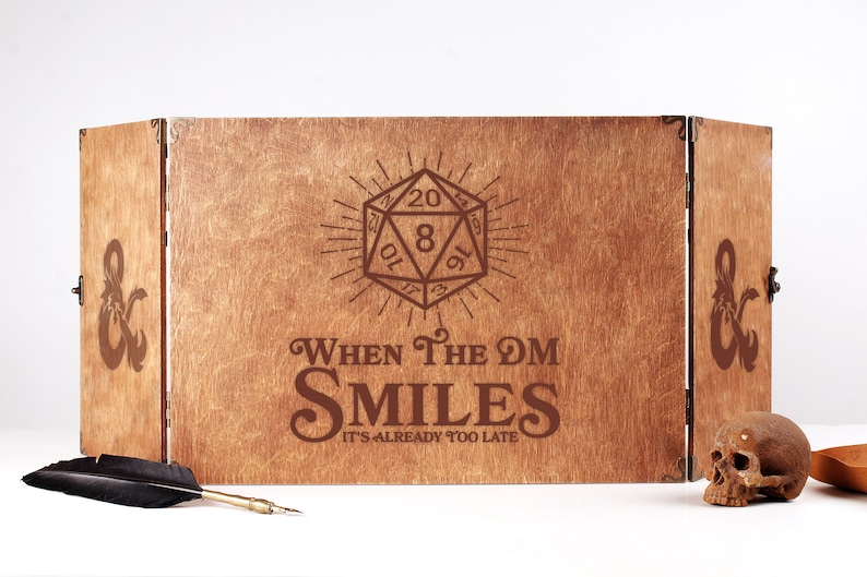 May include: A wooden, three-panel DM screen with the text "When The DM Smiles, It's Already Too Late" and a D20 die graphic. The screen is brown with dark brown etched designs. A skull, feather, and pen are in the foreground.