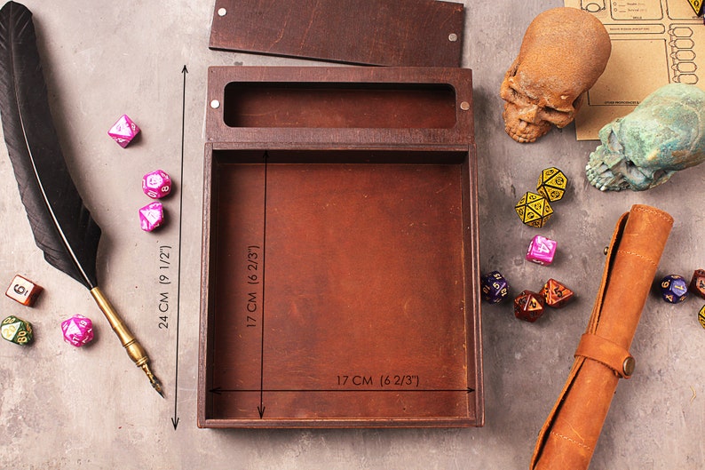 May include: A wooden box with a lid, measuring 17 inches by 17 inches, for storing and rolling dice. The box is made of brown wood and has a brown leather interior. The box is surrounded by dice and a quill pen.