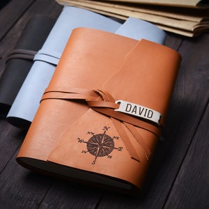 May include: A brown leather journal with a compass design and a metal tag that says "DAVID". The journal is tied with a brown leather strap.