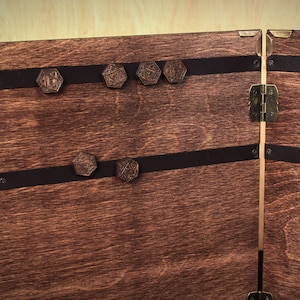 May include: Wooden chest with a dark stain, featuring decorative metal accents and leather straps. The chest is adorned with several hexagonal, engraved wooden pieces. The hinges and clasps are made of brass.