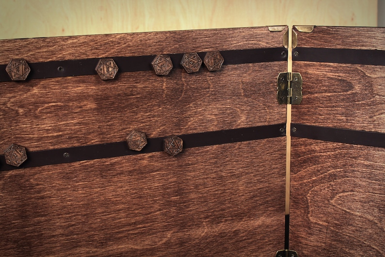 May include: Wooden chest with a dark stain, featuring decorative metal accents and leather straps. The chest is adorned with several hexagonal, engraved wooden pieces. The hinges and clasps are made of brass.