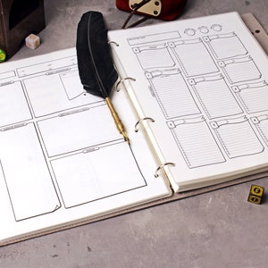 May include: A black and white character sheet for role-playing games, open to a page with a grid of blank lines. A black feather quill pen is resting on the page. The character sheet is in a binder with a brown cover.