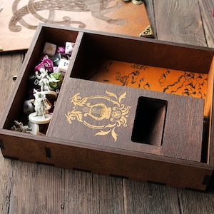 May include: A wooden box with a hinged lid, containing dice, miniature figures, and a map. The box has a decorative design on the front and a compartment for storing dice.