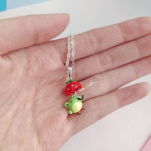 Pu&ograve; includere: Una collana con catena d'argento con un ciondolo a forma di rana verde che tiene un ombrello rosso con pois bianchi.