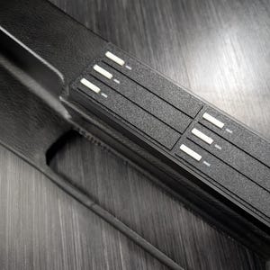 Può includere: Pannello di controllo nero con una superficie testurizzata e più pulsanti bianchi.