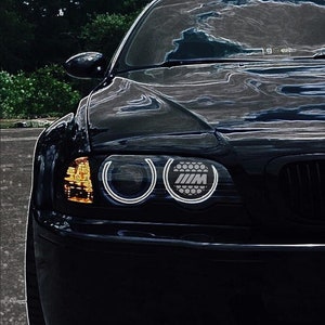 May include: A black BMW M3 with round headlights and a black grille. The car has a silver "M" logo on the front.