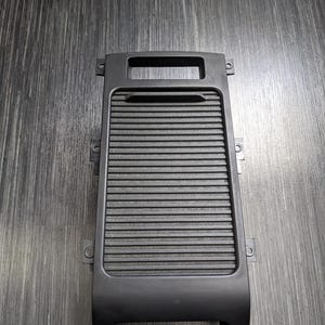 May include: Black plastic car part with a rectangular opening and a series of horizontal lines. The part has a curved bottom and several small holes on the sides.