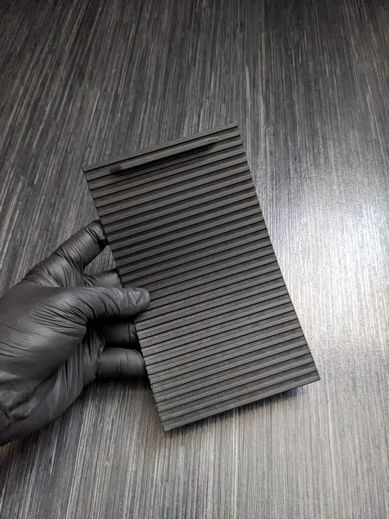 May include: Black plastic car vent cover with a ribbed texture. The cover is designed to fit over a car's air vent to block airflow.