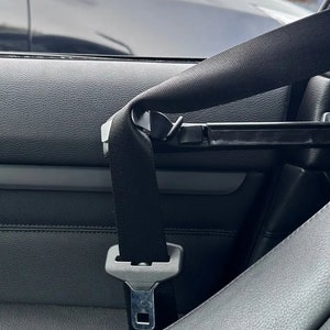Puede incluir: Un cinturón de seguridad de coche negro está abrochado y asegurado en un coche. El cinturón de seguridad está retraído y la hebilla es visible.