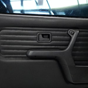 Puede incluir: Panel de puerta de coche de cuero negro con una manija de puerta, un reposabrazos y controles de ventana.