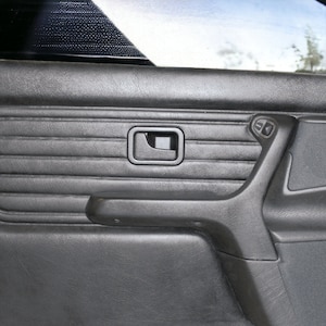 Puede incluir: Panel de puerta de coche de cuero negro con un dise&ntilde;o texturizado, una manija de puerta y una manivela de ventana.