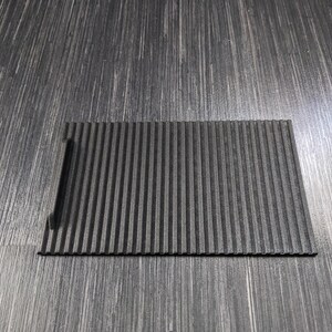 May include: A black, rectangular, ribbed, non-slip mat with a small cutout on the left side.