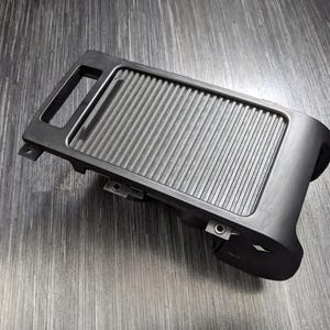 May include: Black plastic car part with a textured surface and a small handle. The part has a rectangular shape and is designed to fit into a car's interior.