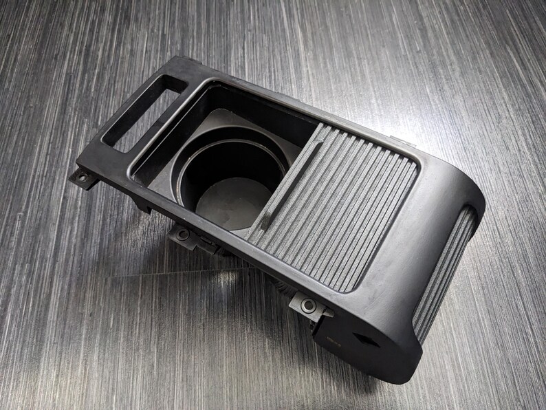 May include: Black plastic car cup holder with a sliding cover. The cup holder has a single cup slot and a sliding cover that reveals a storage compartment.
