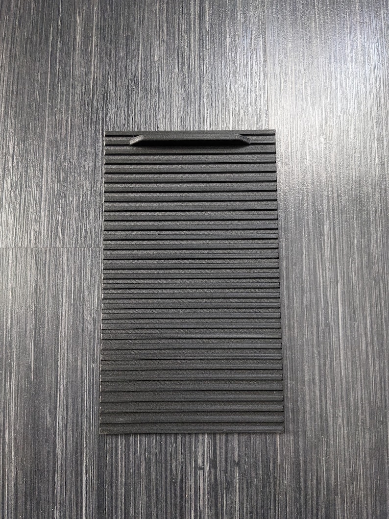 May include: A black plastic vent cover with horizontal lines. The cover has a small handle on the top.