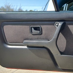 Puede incluir: Primer plano del interior de una puerta de coche negra con un patr&oacute;n a cuadros en el panel de la puerta y una manija de la puerta negra.
