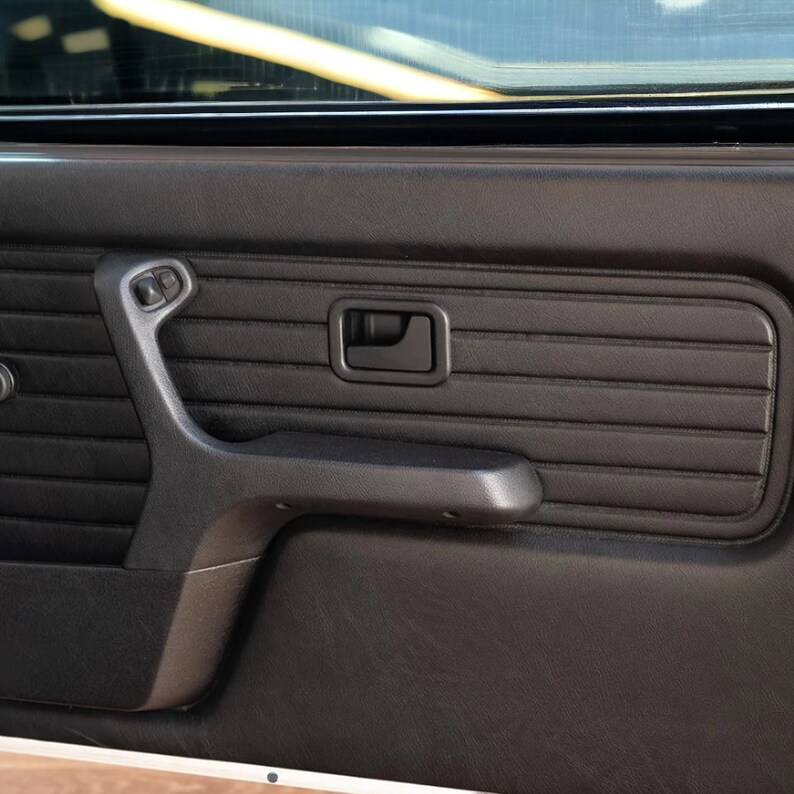 Puede incluir: Panel de puerta de coche de cuero negro con una manija de puerta de pl&aacute;stico negro y un reposabrazos de pl&aacute;stico negro. El panel tiene un dise&ntilde;o texturizado y acolchado.