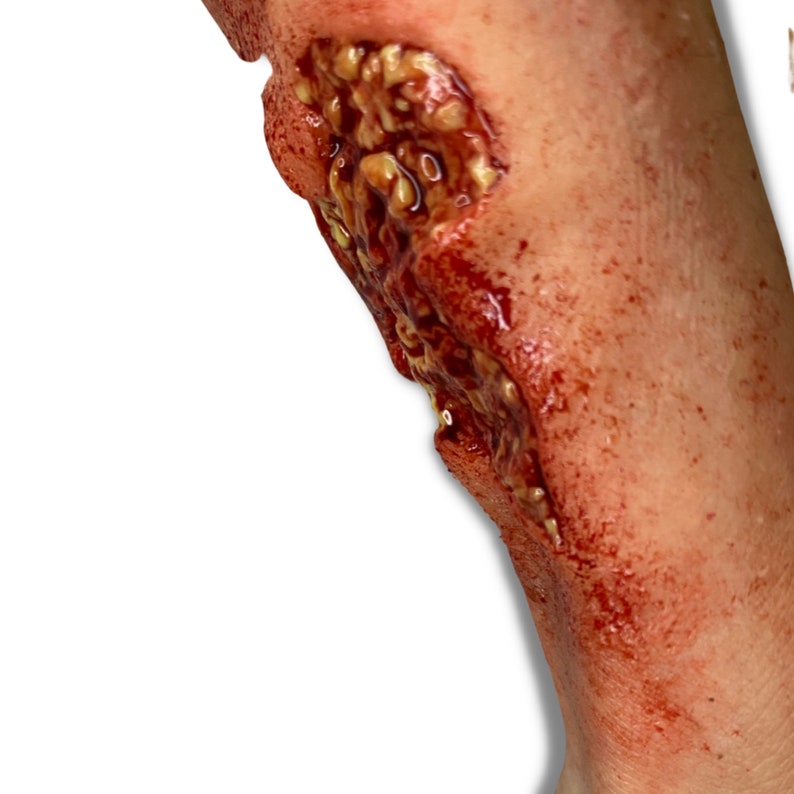 May include: A gruesome, realistic special effects wound. The open wound displays exposed flesh, with a mix of red, brown, and yellow tones. The edges of the wound are ragged, and the overall effect is highly detailed and disturbing.