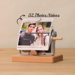 May include: A silver photo album with a wooden base. The album holds 32 photos or videos and has a crank to turn the pages. The album is displaying a photo of a couple.