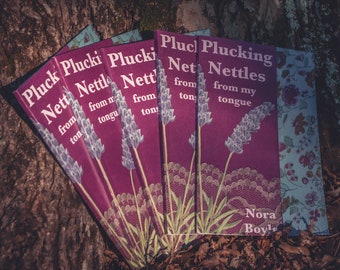 May include: A stack of five books with the title "Plucking Nettles from my tongue" by Nora Boyle. The books have a purple cover with a floral design and a lavender sprig.